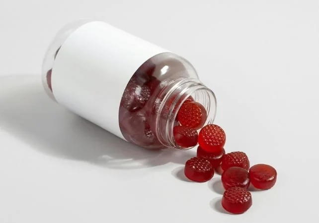 Un flacon en plastique blanc couché sur le côté, d'où s'échappent de petites gommes rouges.