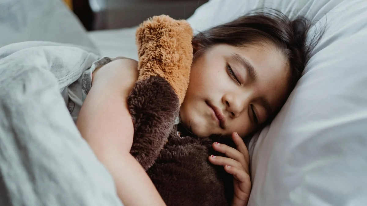 Une jeune fille endormie paisiblement dans son lit avec un ours en peluche.